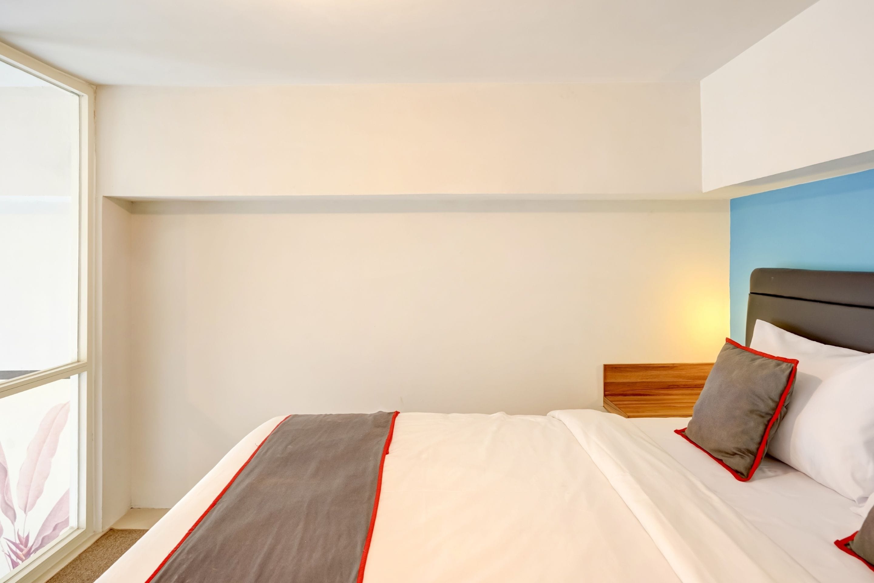 A hotel room with a bed, a headboard, a window, and a wall with a blue accent.
