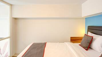 A hotel room with a bed, a headboard, a window, and a wall with a blue accent.