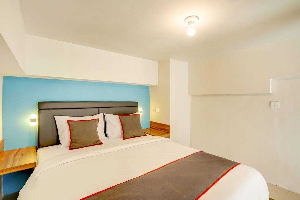 A modern hotel room with a large bed, a wooden nightstand, and a blue accent wall.