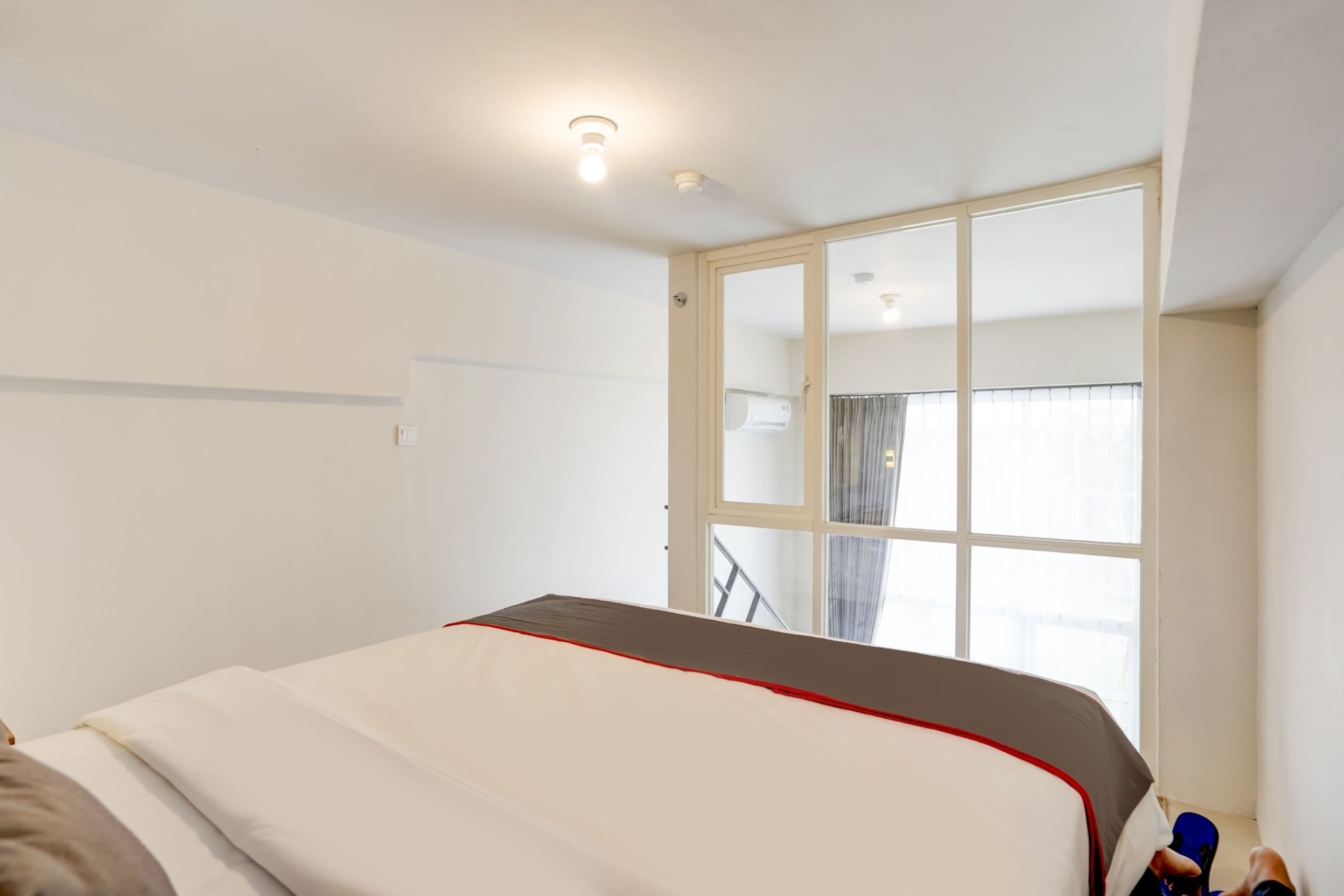 A hotel room with a bed, a window with curtains, and a door leading to a balcony.