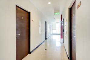 A corridor with doors, an exit sign, and a fire alarm. - Super OYO Collection O 30 Amega Crown Sub (Surabaya)