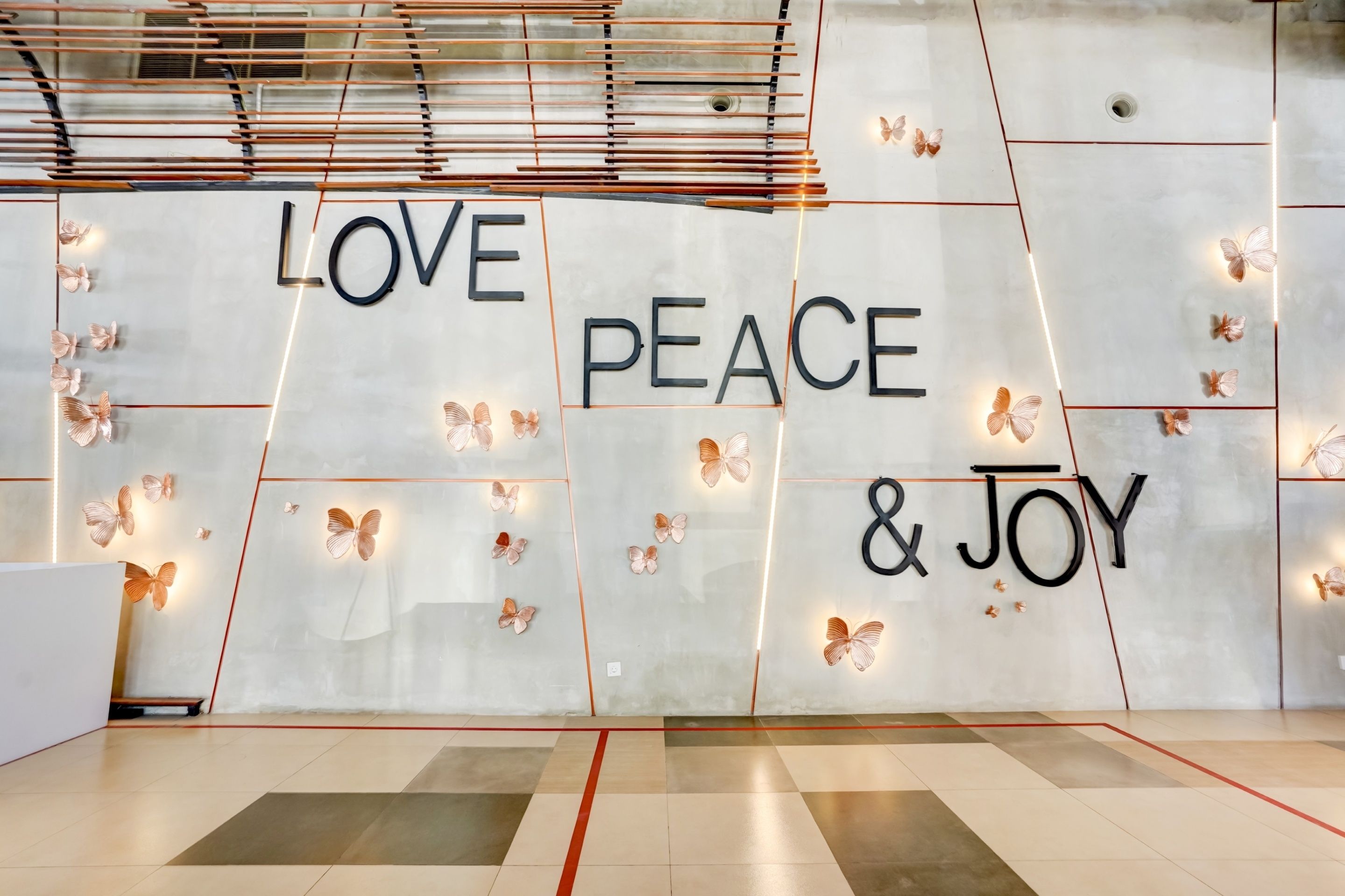 Parede decorada com as palavras 'LOVE PEACE & JOY' e luzes em forma de borboletas.