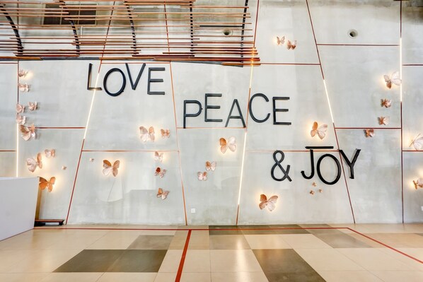 Paret amb les paraules 'LOVE PEACE & JOY' i llums de papallones decoratives.