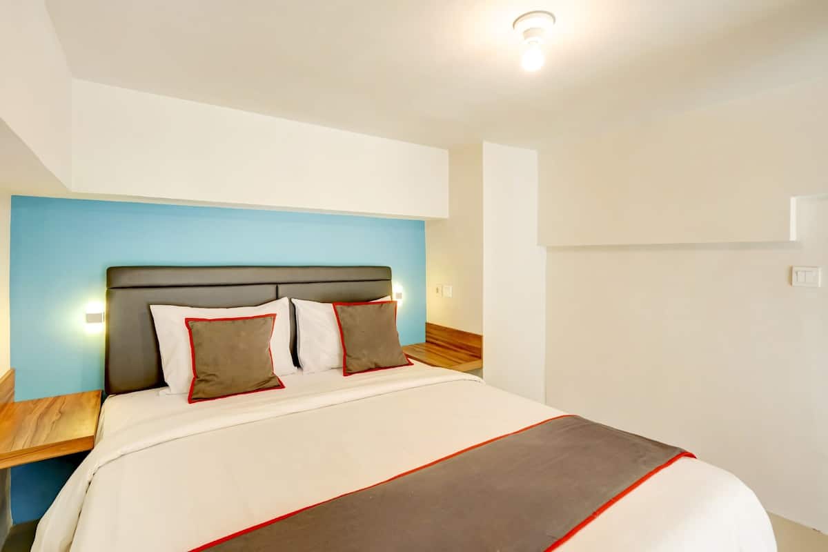 A hotel room with a bed, a nightstand, and a wall-mounted light.