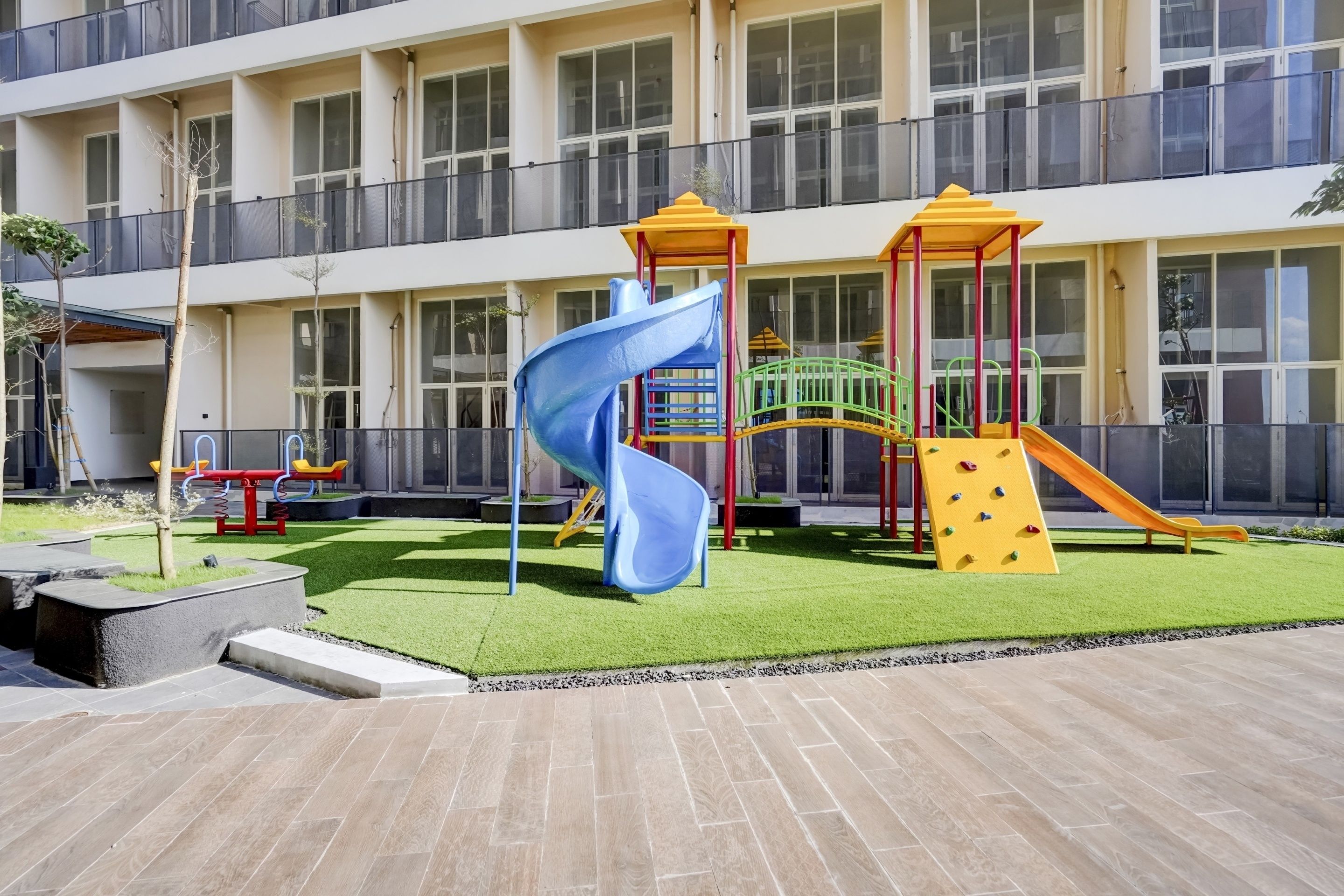 Une aire de jeux avec un toboggan bleu et des structures d’escalade, entourée d’un bâtiment doté de grandes fenêtres.