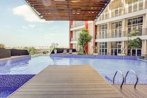 A rooftop swimming pool with wooden deck, lounge chairs, and a modern building with large windows. - Super OYO Collection O 30 Amega Crown Sub (Surabaya)