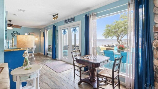 Een interieur van een strandhuis met een eethoek en uitzicht op zee, met een bord waarop 'BEACH HOUSE' staat.