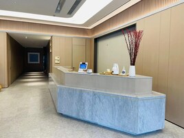 Un mostrador de recepción con un quiosco digital, un jarrón con ramas rojas y una bandeja de madera con artículos de cortesía.