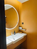 Un baño moderno con un lavamanos blanco, un espejo redondo con marco blanco y una pared de madera.