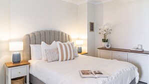 A neatly arranged bedroom with a large bed, bedside lamps, a nightstand, a dresser, and a vase with flowers. - Namanula Unit 6 - Ocean Views & Walk to Convent Beach - Holiday Yamba (Yamba)