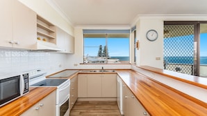 A modern kitchen with a view of the sea, a clock on the wall, and a balcony with a mesh screen. - Namanula Unit 6 - Ocean Views & Walk to Convent Beach - Holiday Yamba (Yamba)