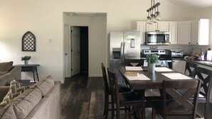Uma cozinha moderna com eletrodomésticos de aço inoxidável, uma sala de jantar com mesa e cadeiras de madeira, e uma sala de estar acolhedora com sofá e almofadas decorativas.