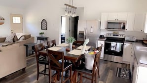 Cozinha moderna com armários brancos, eletrodomésticos de aço inoxidável e uma área de jantar com cadeiras e mesa de madeira.