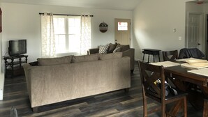 Uma sala de estar com sofá, televisão, mesa de jantar com cadeiras e janela com cortinas.