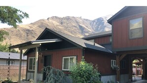 Uma casa de dois andares com fachada vermelha, varanda coberta e montanhas ao fundo.