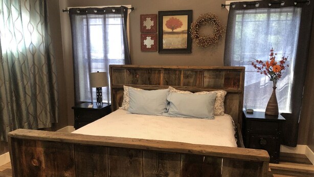 Um quarto com uma cama de madeira, duas mesas de cabeceira, uma luminária na parede e um vaso com flores.