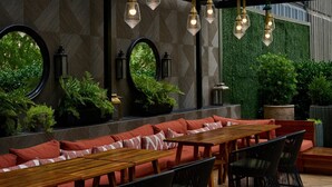 An outdoor seating area with round tables and red cushioned benches, surrounded by greenery and decorative lighting. - The Starling Atlanta Midtown, Curio Collection by Hilton (Atlanta)