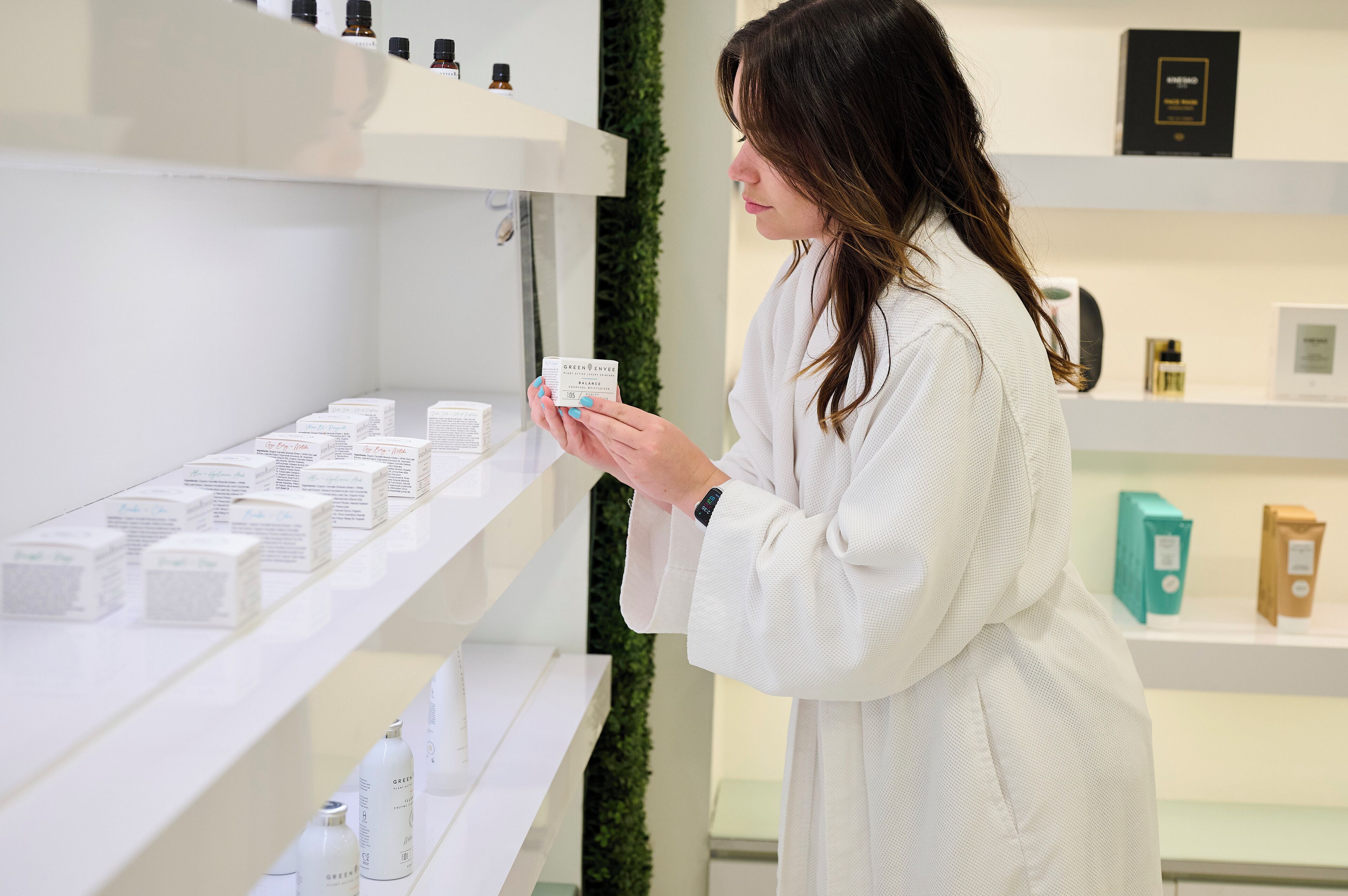 Une personne vêtue d’une robe blanche examine des produits exposés sur des étagères dans un espace de vente moderne et bien éclairé.