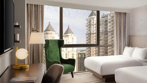 A hotel room with a bed, a desk with a lamp, a chair, and a large window offering a city view. - The Starling Atlanta Midtown, Curio Collection by Hilton (Atlanta)