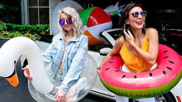 Two individuals holding inflatable swan and watermelon floats.
