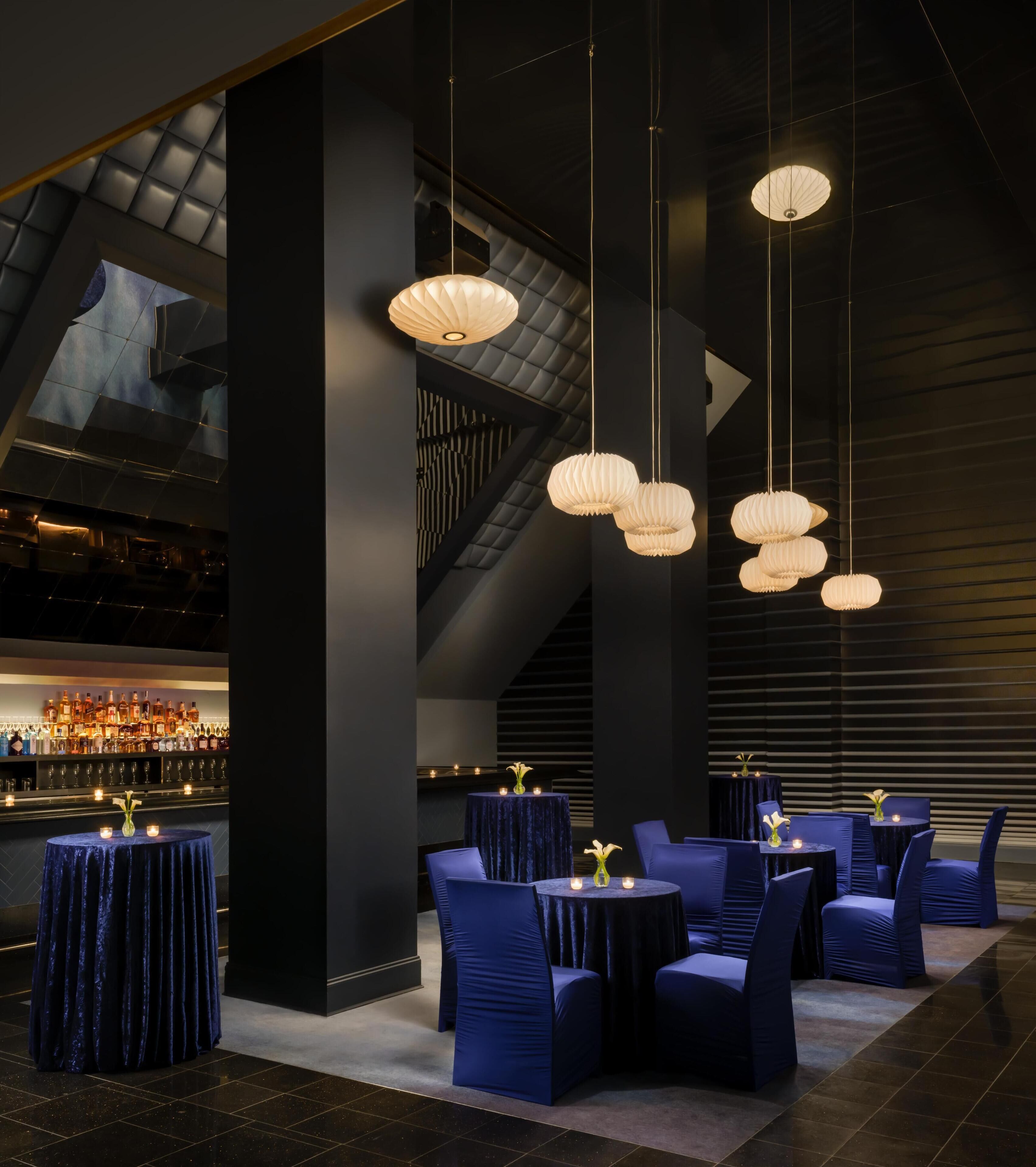 A modern bar area with tiered seating and hanging paper lanterns.