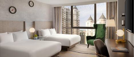 A hotel room with two beds, a green armchair, a desk with a lamp, and a TV.