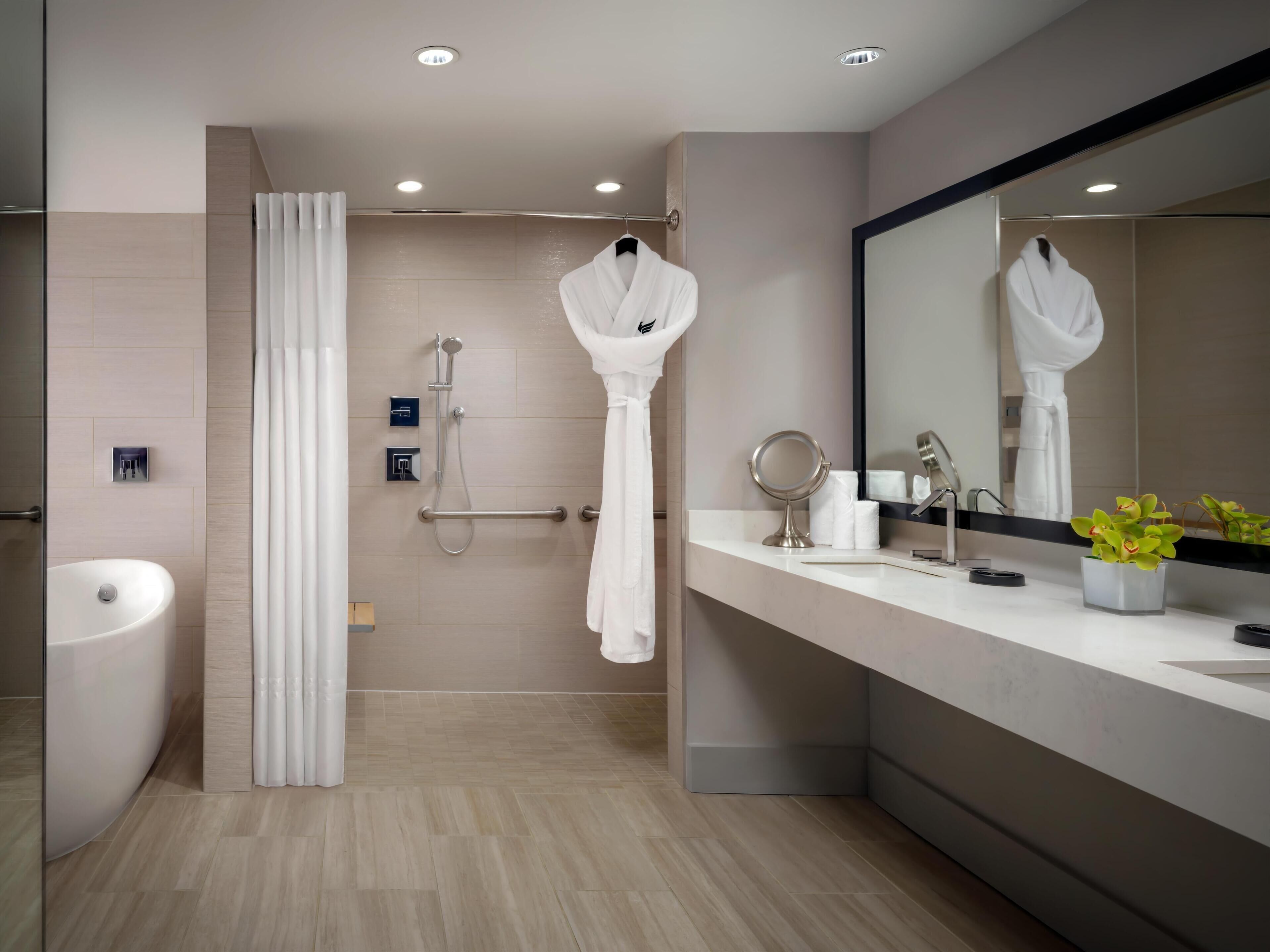 A modern bathroom with a bathtub, a shower with a handheld showerhead, a vanity with a mirror, and a potted plant.