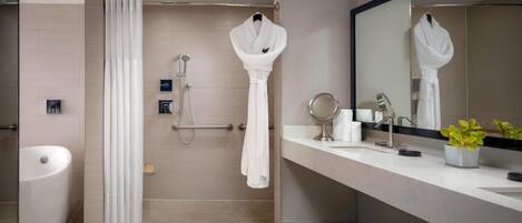 A modern bathroom with a bathtub, a shower with a handheld showerhead, a vanity with a mirror, and a potted plant.