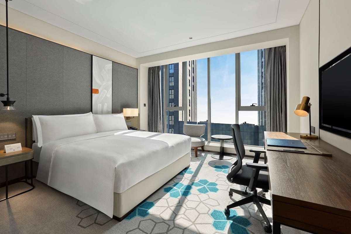 A modern hotel room with a large bed, a desk, a chair, and a TV.