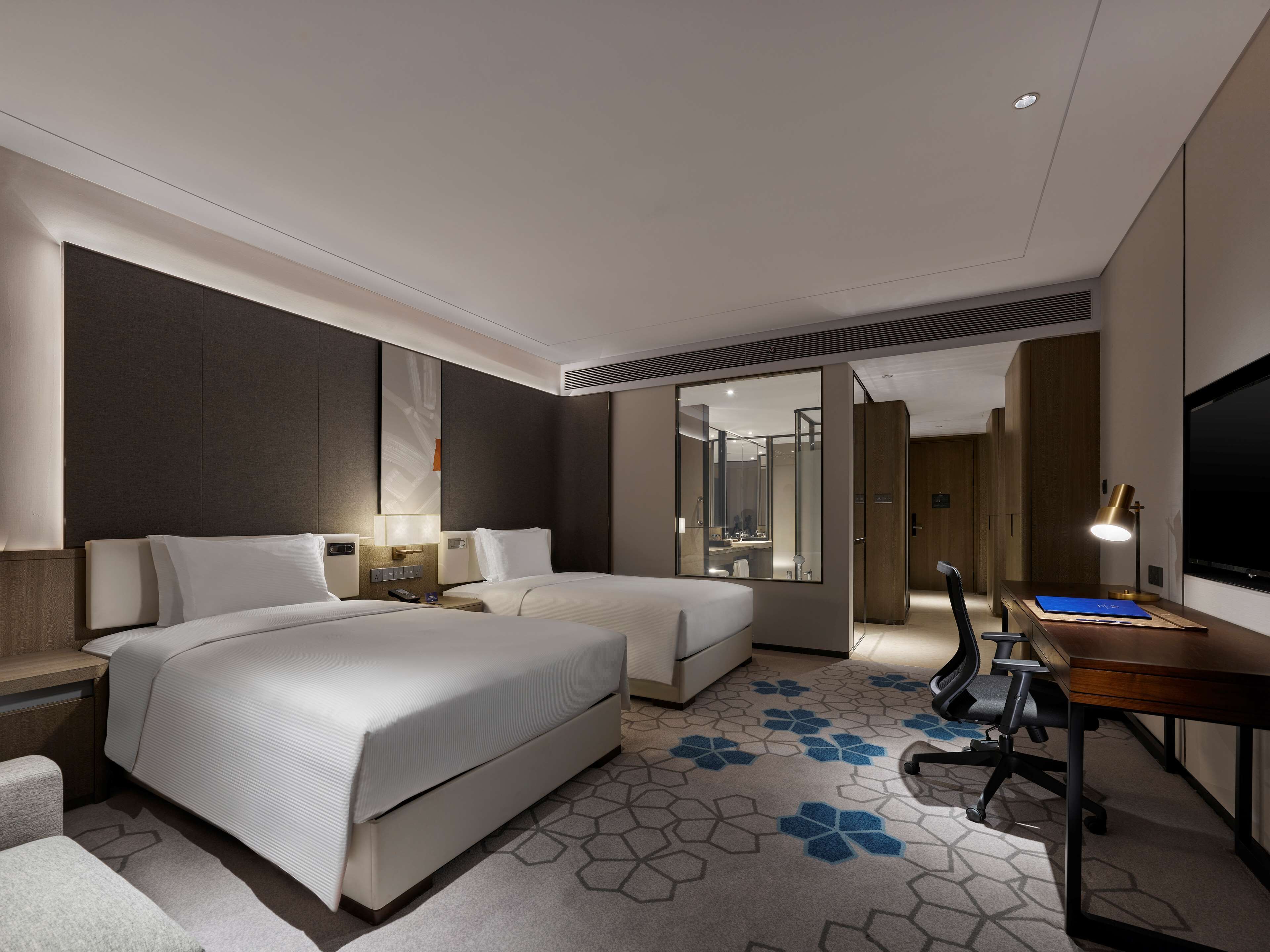 Una habitación de hotel moderna con dos camas, un escritorio, una silla, un televisor y un espejo grande.