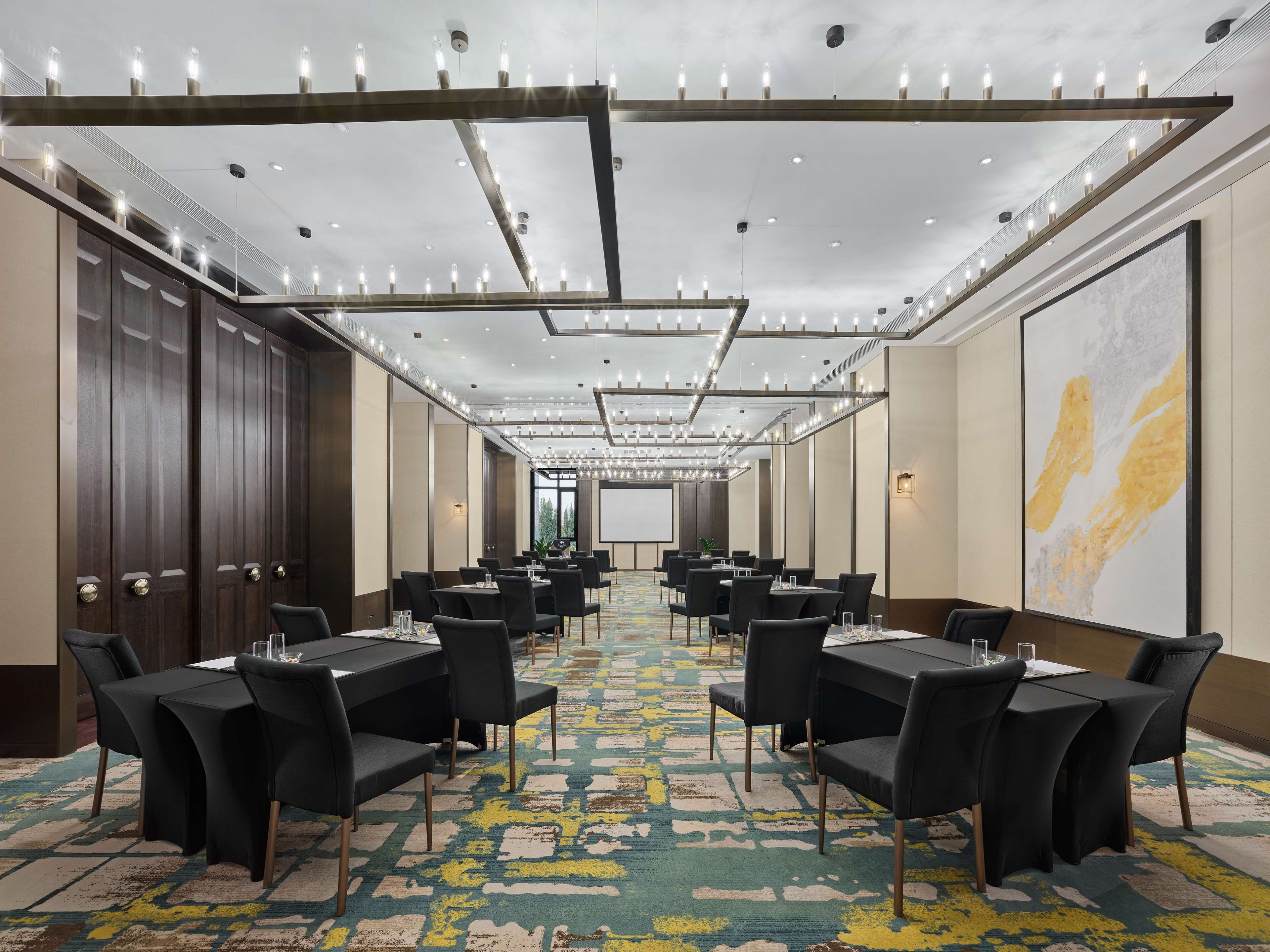A conference room with multiple tables and chairs, a patterned carpet, and a large abstract painting on the wall.