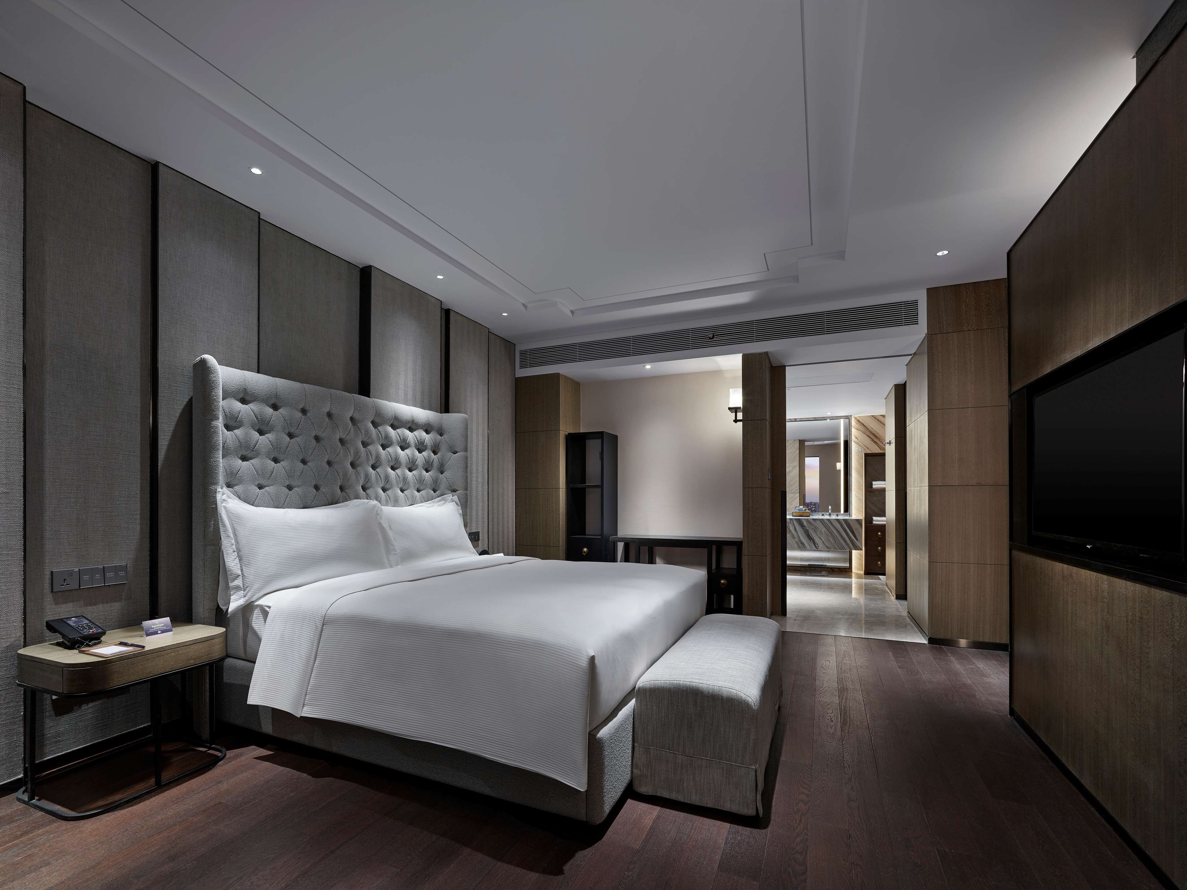 A modern hotel room with a large bed, bedside table, and a flat-screen TV.