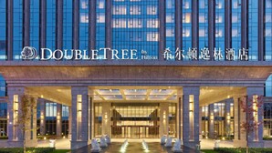 L’entrée d’un hôtel DoubleTree by Hilton, caractérisée par un design moderne, de grandes fenêtres en verre et une façade bien éclairée.