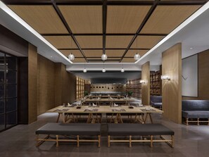 A modern dining area with a long table, benches, and a kitchen in the background.