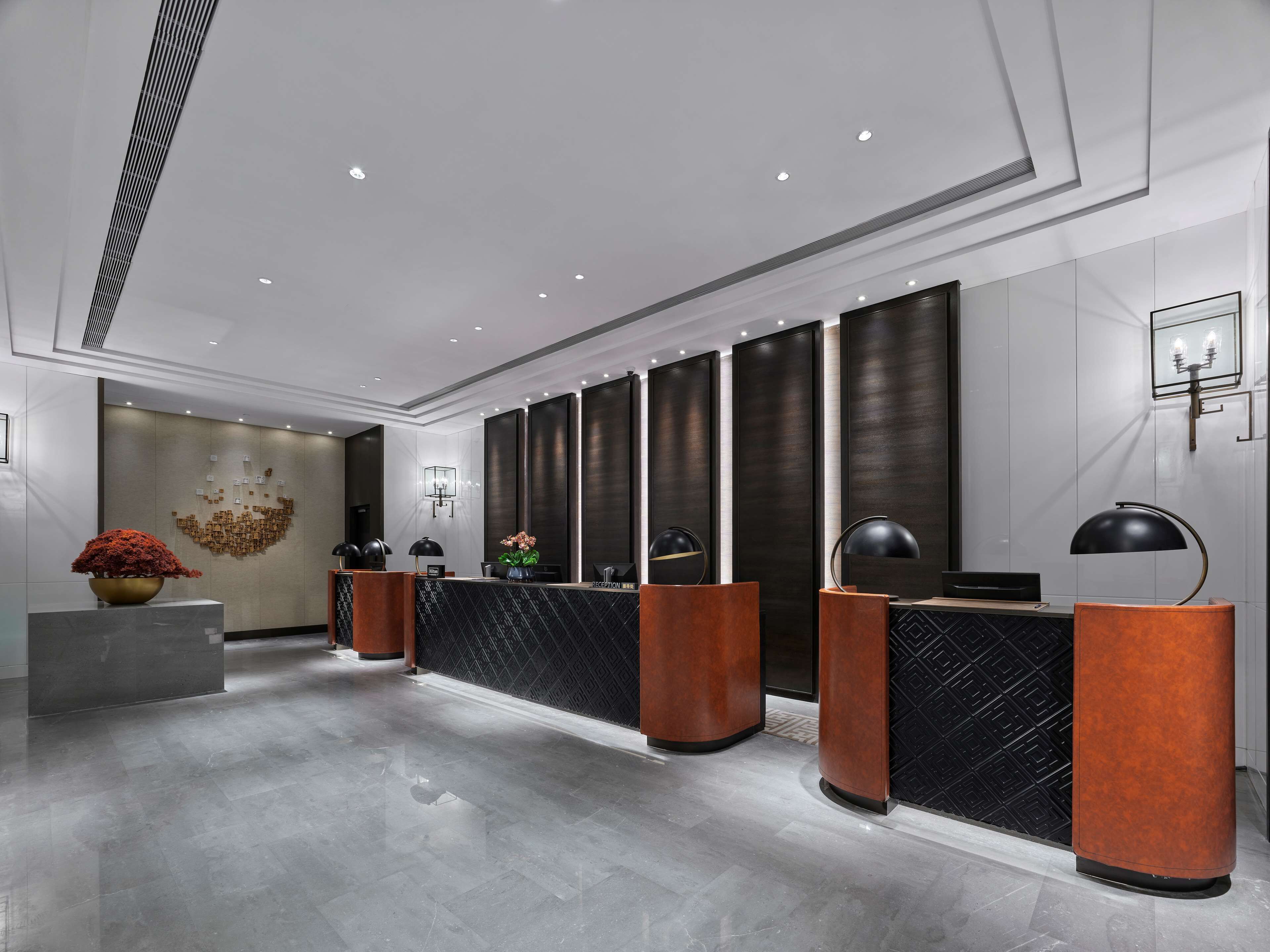 A modern reception area with a marble floor, dark wood paneling, and a central reception desk with a black countertop and wooden base.