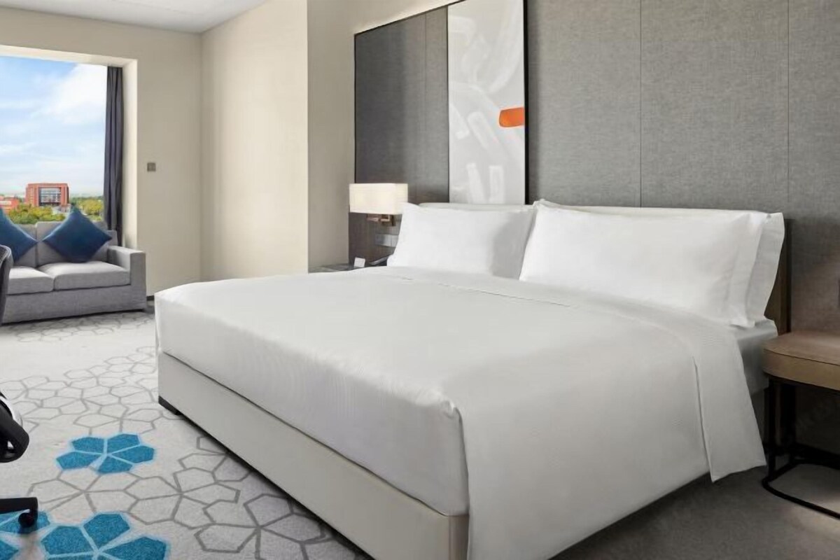 Habitación de hotel con una cama grande, un sofá, un escritorio con lámpara y vistas a la ciudad.