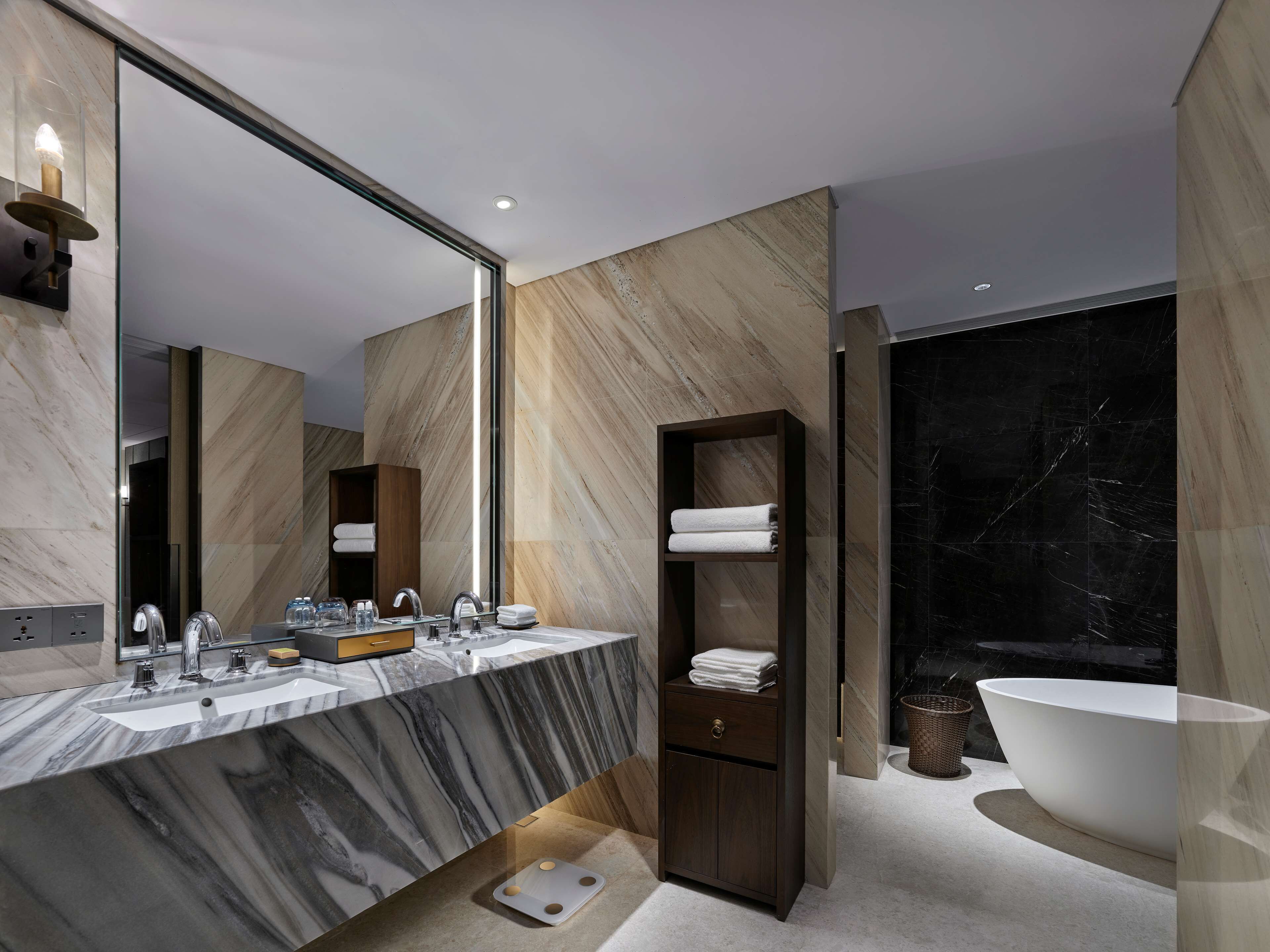Un baño moderno con tocador de mármol, un espejo grande, una pared de mármol oscuro y una bañera independiente.