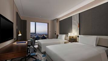 Une chambre d’hôtel avec deux lits, un bureau, une télévision et une grande fenêtre donnant sur la ville.