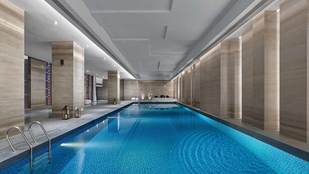 Une piscine intérieure moderne, avec une eau d’un bleu limpide, entourée de murs en panneaux de bois et dotée d’un plafond avec des luminaires encastrés.
