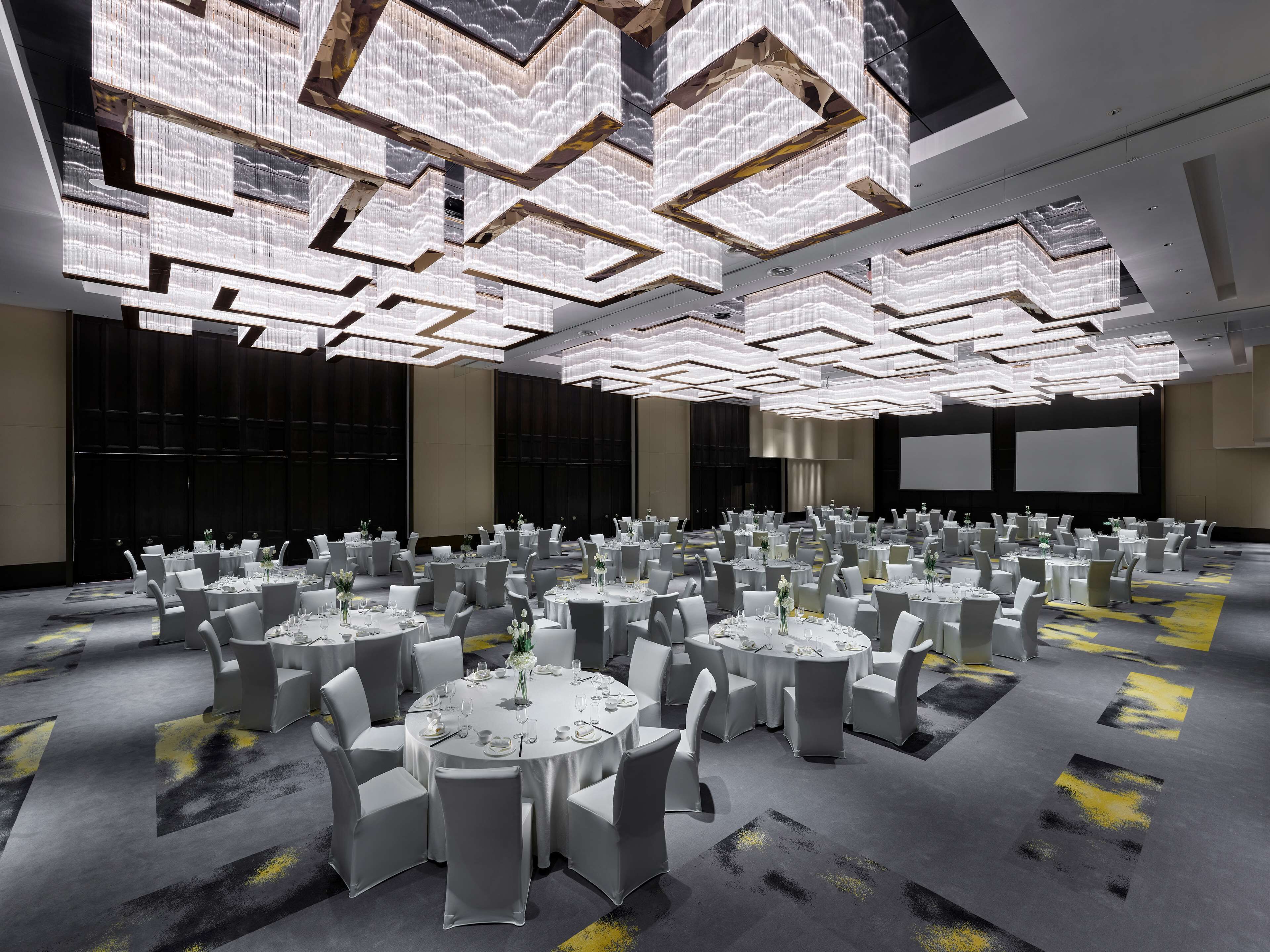 A conference room with multiple round tables, white chairs, and a modern ceiling design.