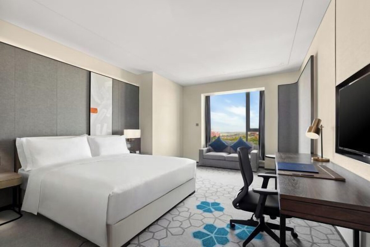 Una habitación de hotel moderna con una cama grande, un escritorio, una silla y un televisor.