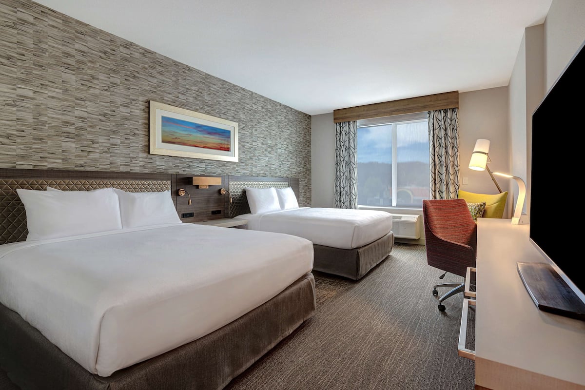 A hotel room with two beds, a desk, a TV, and a window with curtains.