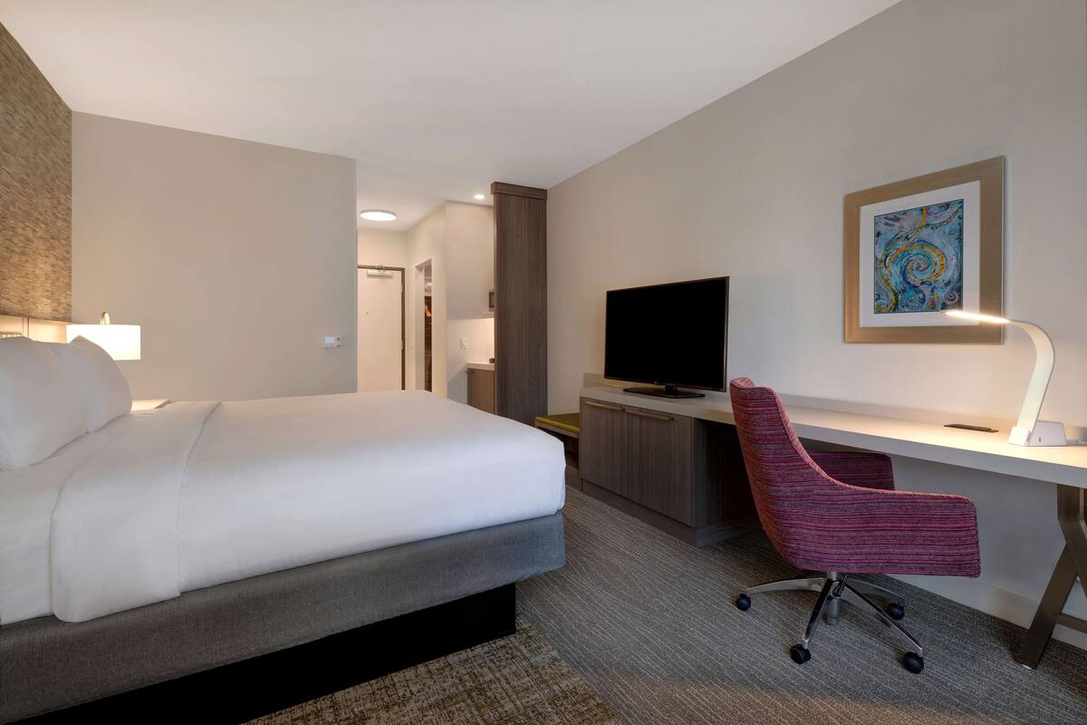 A hotel room with a bed, a desk with a chair, a television, and a framed artwork on the wall.