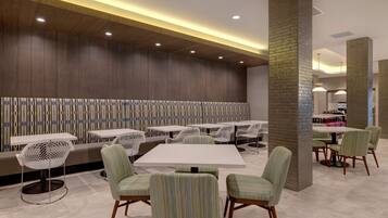 Un restaurante moderno con mesas y sillas altas, un pared con diseño y una columna de ladrillo.