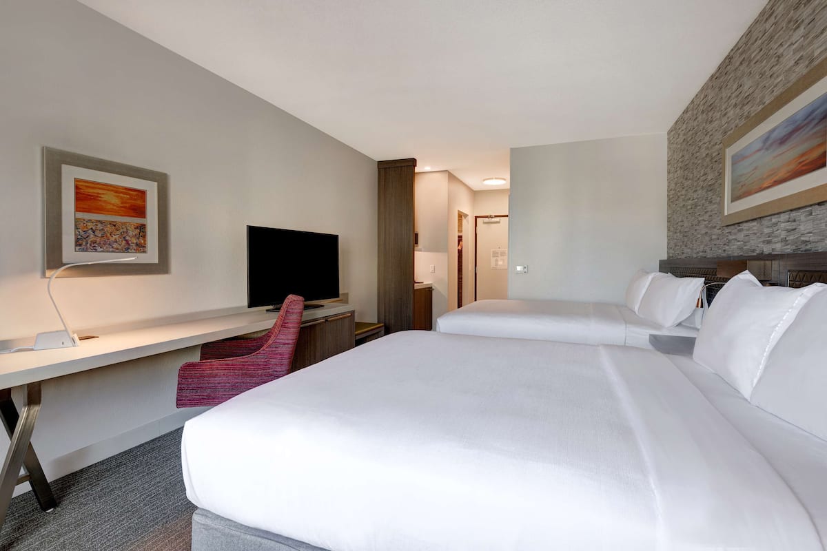 A hotel room with two beds, a desk, a TV, and artwork on the walls.