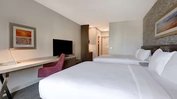 A hotel room with two beds, a desk, a TV, and artwork on the walls.