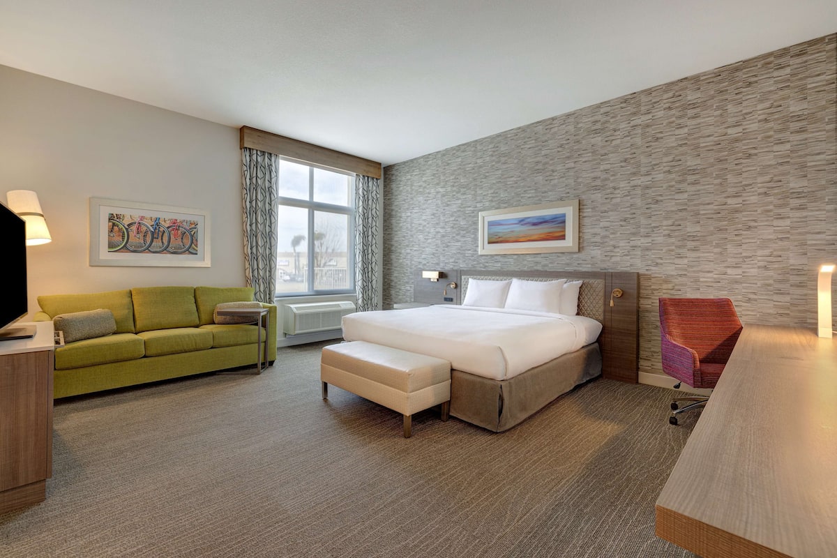 A hotel room with a bed, a green sofa, a desk, and a window with curtains.