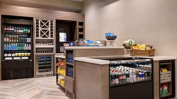 A self-service beverage station with refrigerated and non-refrigerated drink options, snack bars, and a seating area with a wooden design.