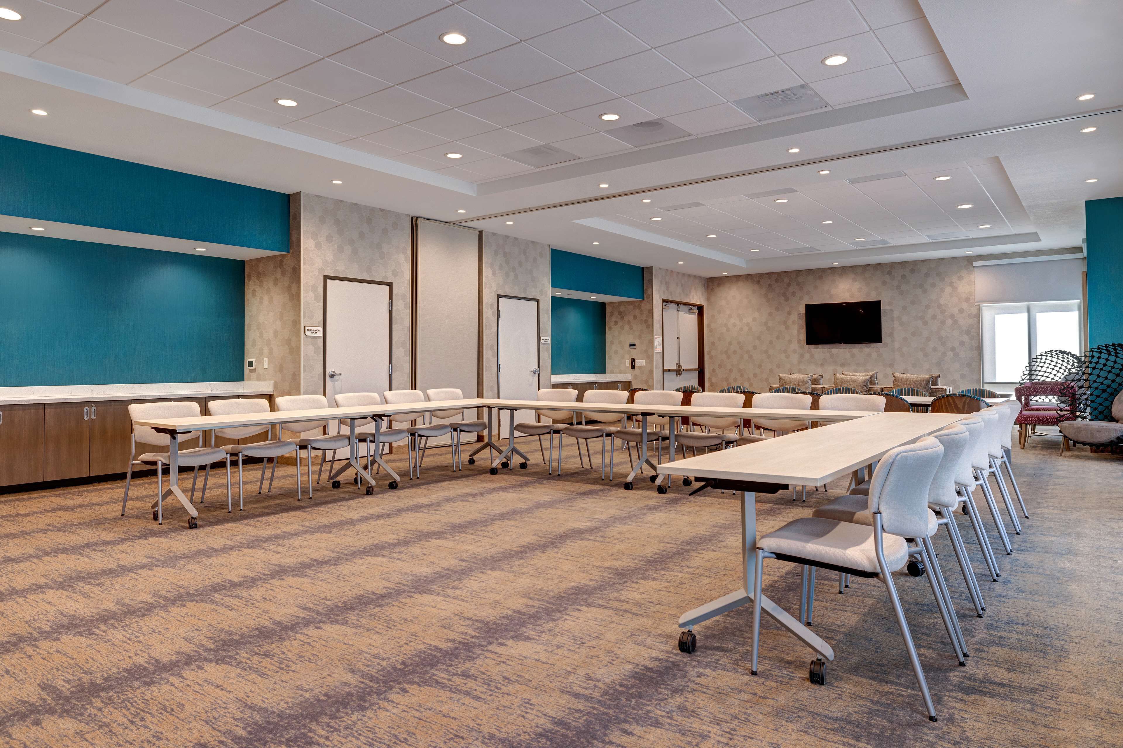 A conference room with a long table, chairs, and a TV screen.