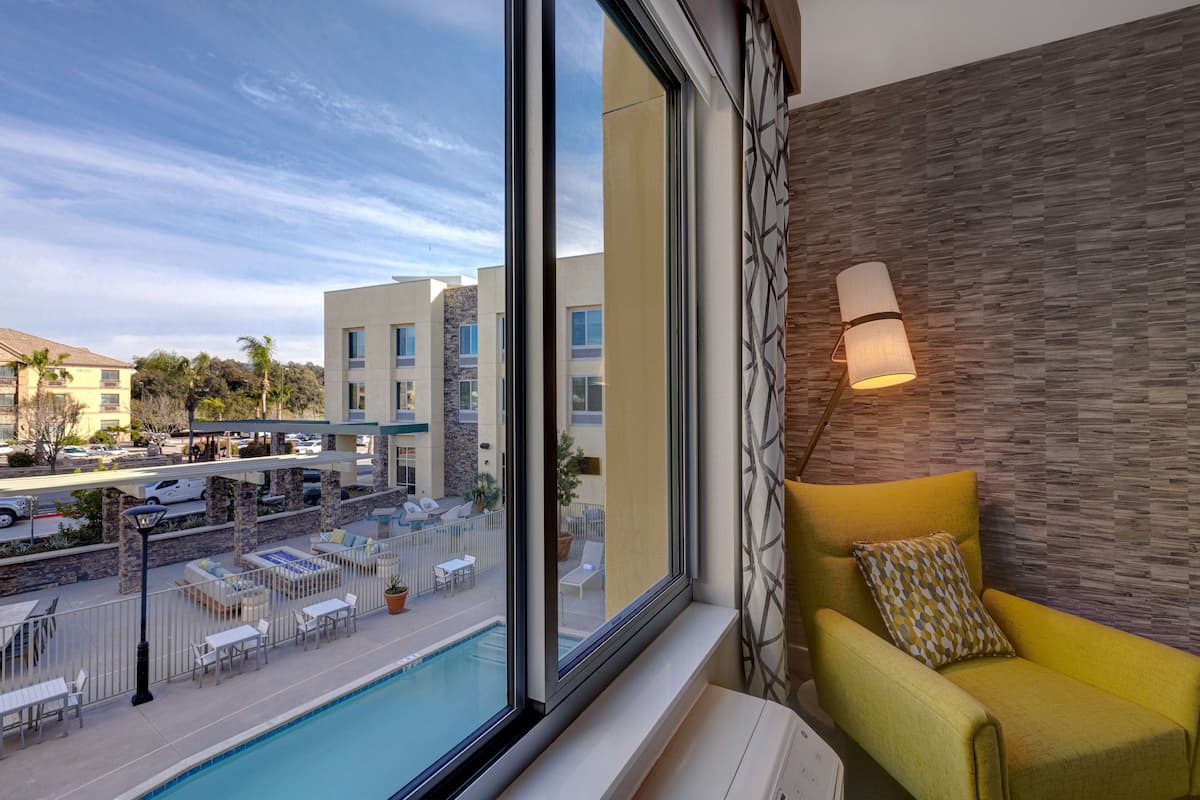 A hotel room with a large window, a yellow armchair, a pool view, and a modern wall design.